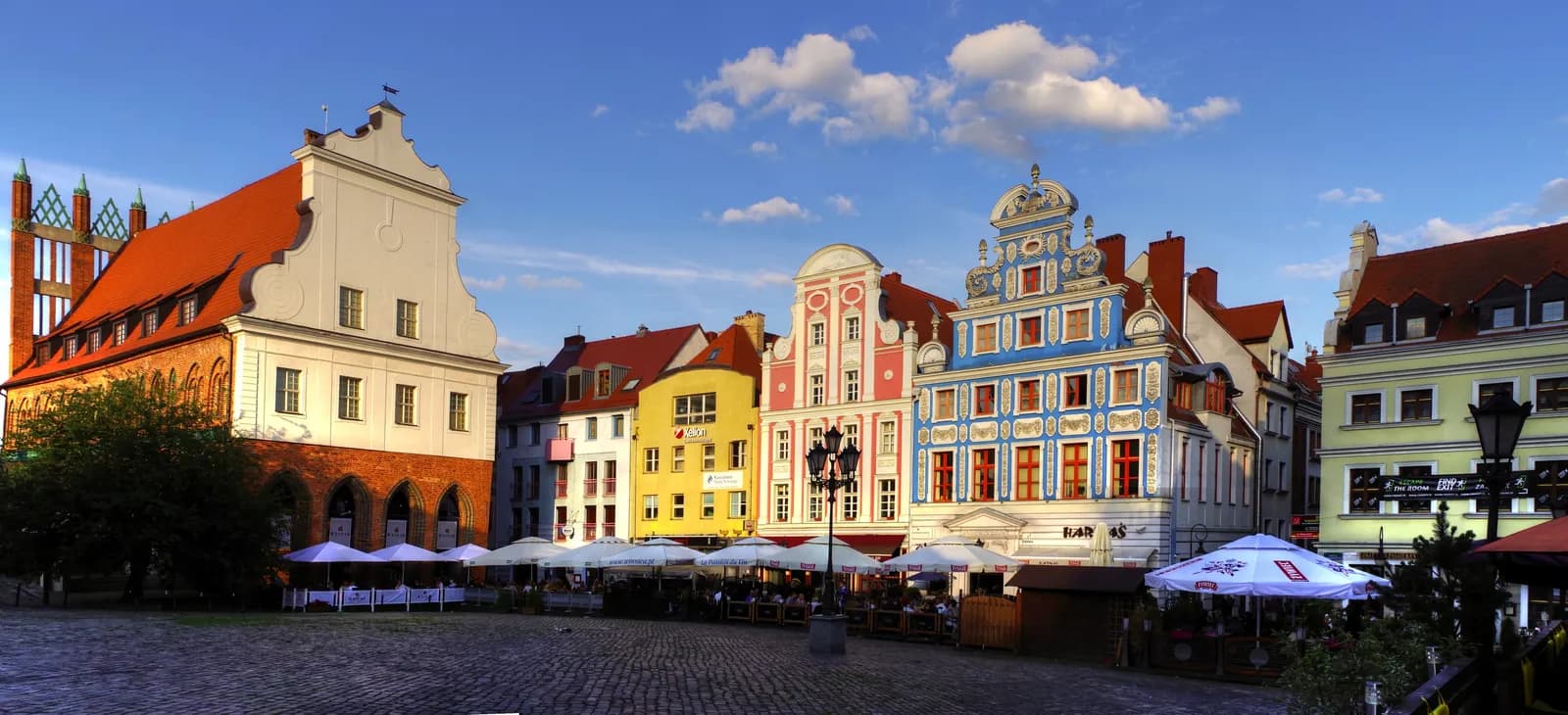 A picturesque European town square with historical buildings in vibrant colors under a clear sky with scattered clouds.